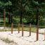 Poręcze gimnastyczne zainstalowane na placu zabaw na piasku, otoczone drzewami.