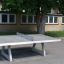 Wolnostojacy stół do tenisa stołowego 11707 zainstalowany na terenie szkolnego boiska.