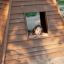 Drewniany Wigwam z uśmiechniętym dzieckiem w oknie na placu zabaw.