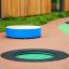 Trampolina okrągła 100 cm z zieloną siatką i czarną osłoną na gumowej powierzchni placu zabaw.