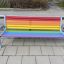 Kolorowa ławka z metalową konstrukcją i drewnianymi deskami w kolorach tęczy na plac zabaw.