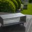 Stolik kawowy z betonu InsideOut Concrete na drewnianym tarasie z zielonym ogrodem w tle.