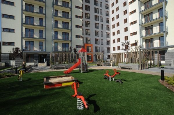 Plac zabaw z systemem amortyzującym ze sztuczną trawą 45 mm w miejskim osiedlu mieszkalnym.
