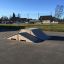 Skatepark z drewnianą rampą na asfaltowym placu.