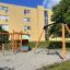 Drewniany plac zabaw Kiosk z huśtawką i zjeżdżalnią przed budynkiem.