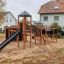 Drewniany plac zabaw Odkrywca z zjeżdżalnią i wieżą obserwacyjną na podwórku.